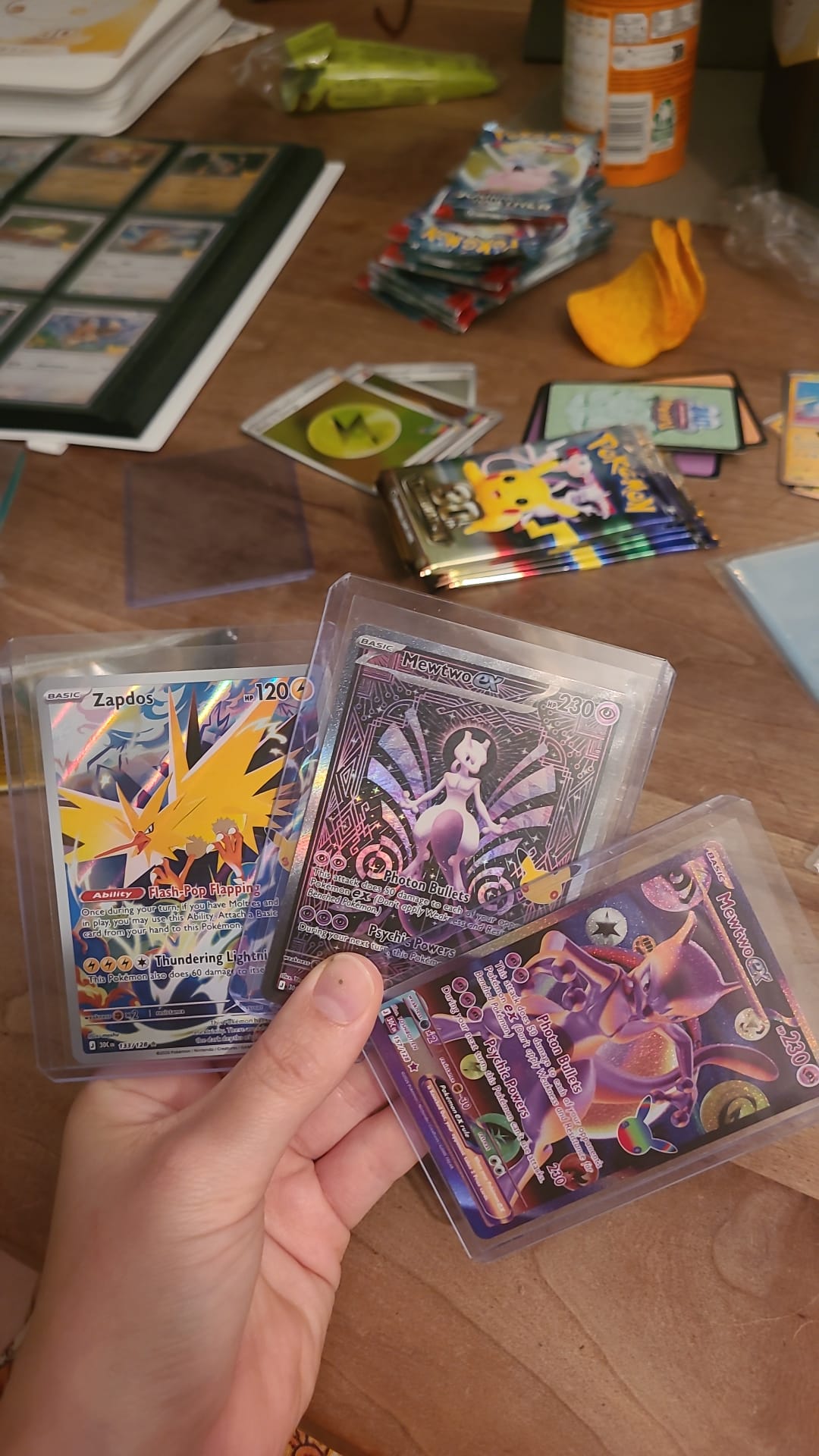 Drie getrokken Pokémon-kaarten in beschermhoesjes, met geopende packs en een binder op tafel